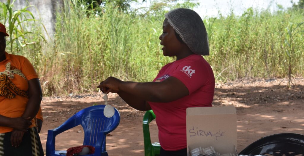 A ativista comunitária Aruquia demonstra como usar preservativos femininos em segurança aos membros da comunidade que aguardam as suas consultas privadas de SSR.