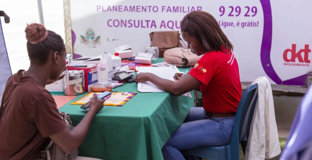 No interior da tenda de consulta da clínica móvel, uma enfermeira regista um jovem doente que procura serviços.